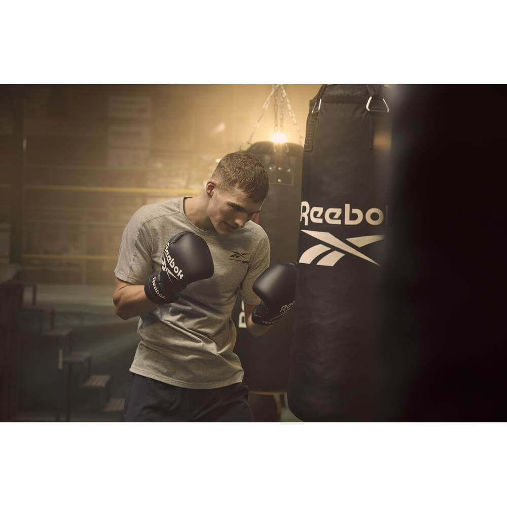 Man punching a Reebok punch bag wearing Reebok Boxing Gloves - Black