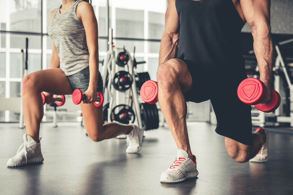 Man and woman performing lunges whilst holding dumbbells in the gym