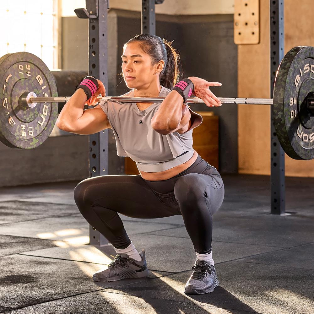 Woman performing a squat with a barbell in a gym setting wearing  adidas wrist wraps