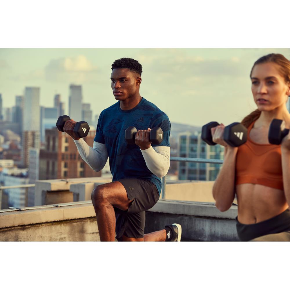 Two people exercising with dumbbells on a rooftop with a cityscape background