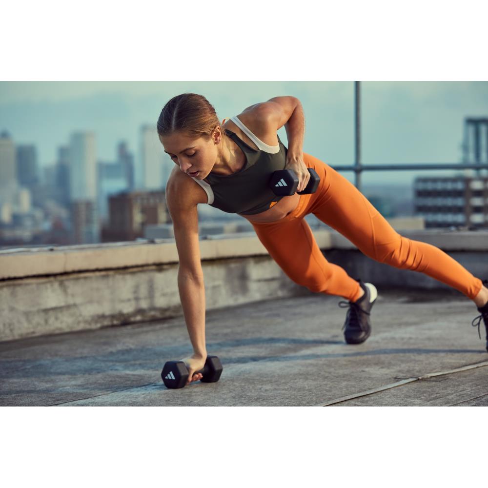 Woman exercising with 3kg dumbbells on a rooftop with cityscape background
