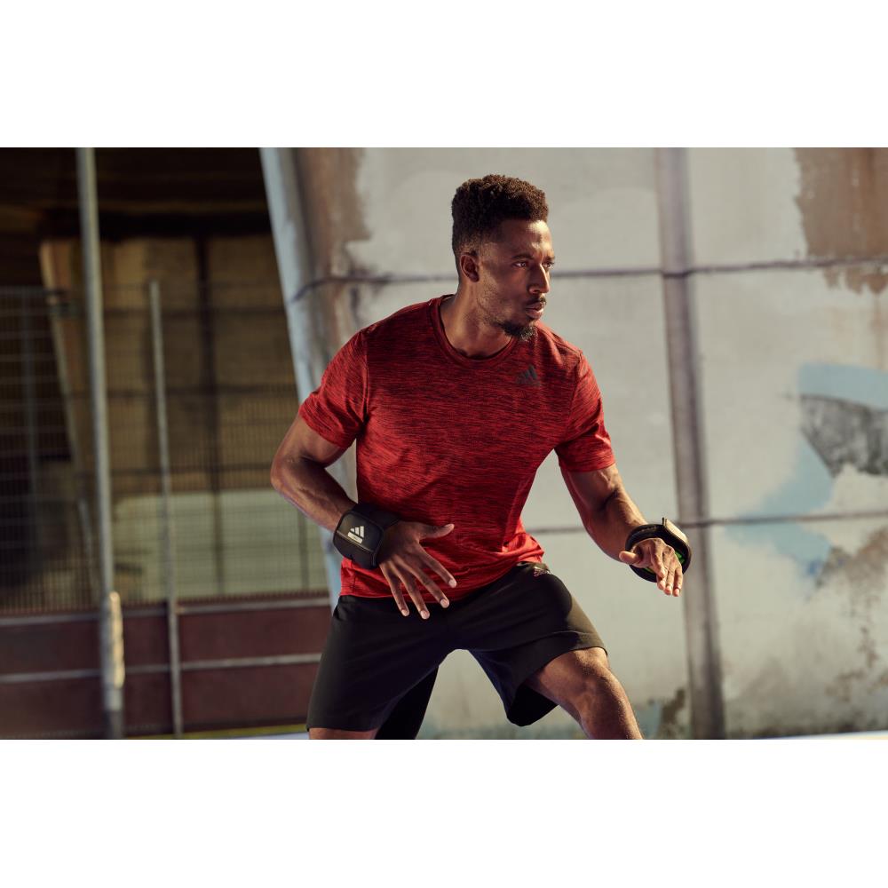 Man in red athletic shirt and black shorts exercising outdoors with the 1.5kg adidas wrist weights