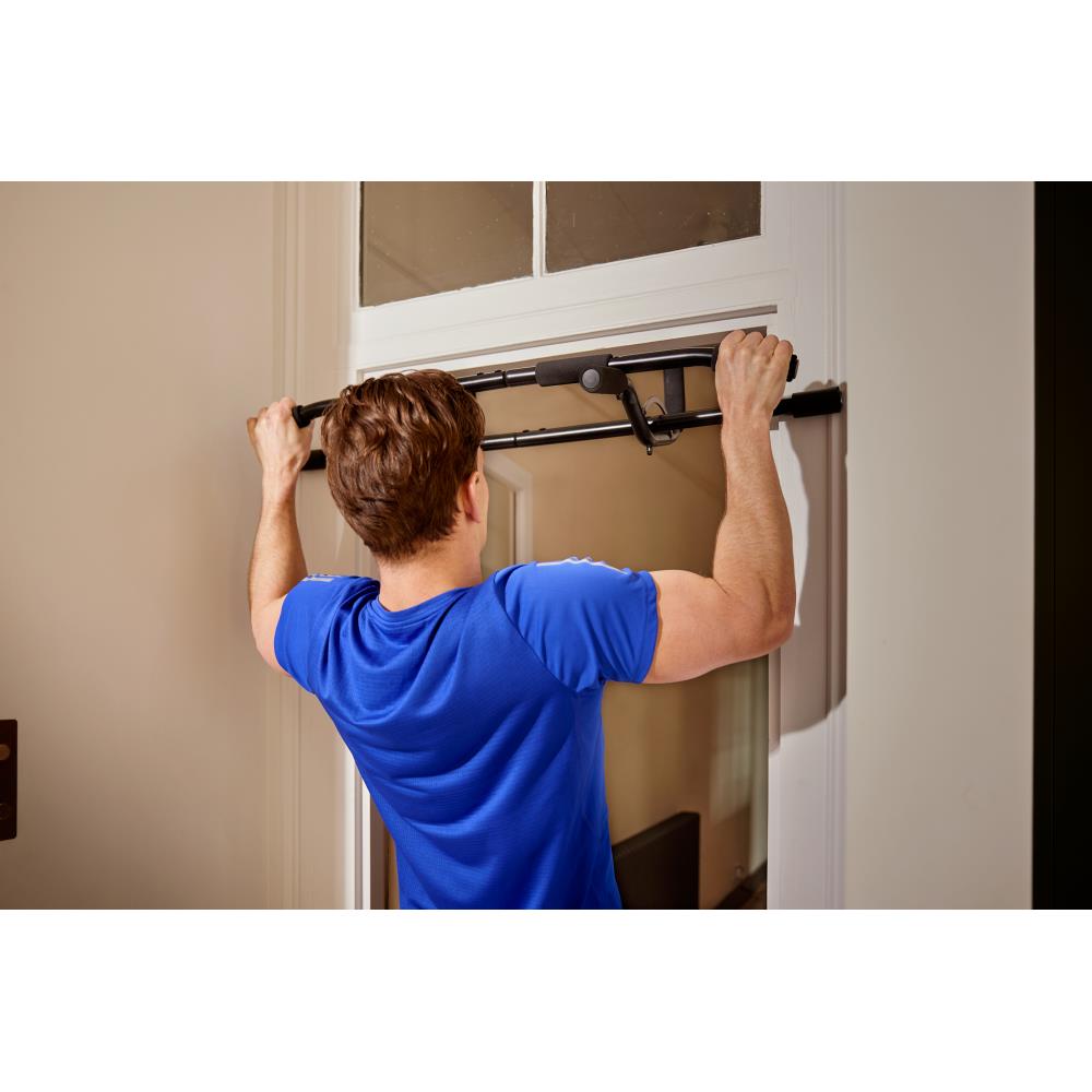 Person using a pull-up bar attached to a door frame in a home setting.