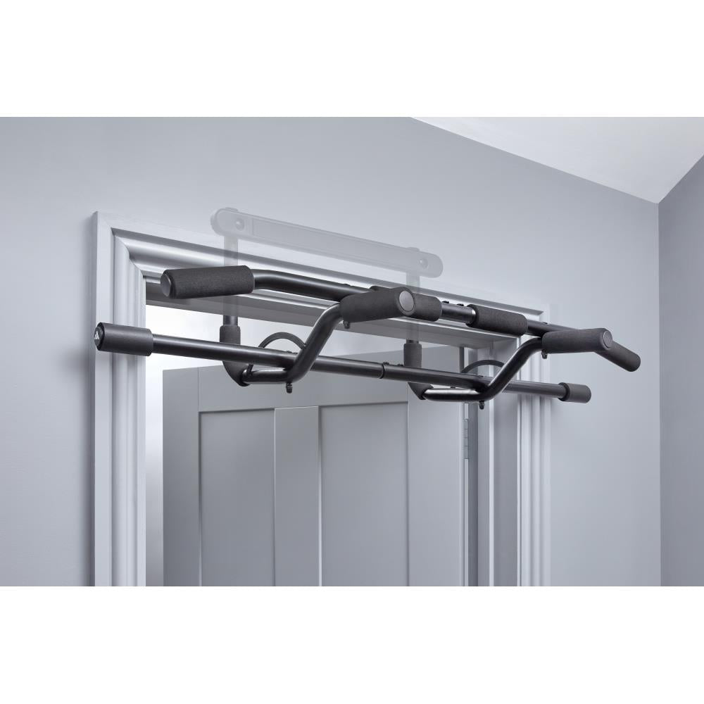 Black adidas pull-up bar attached to a door frame against a grey wall.