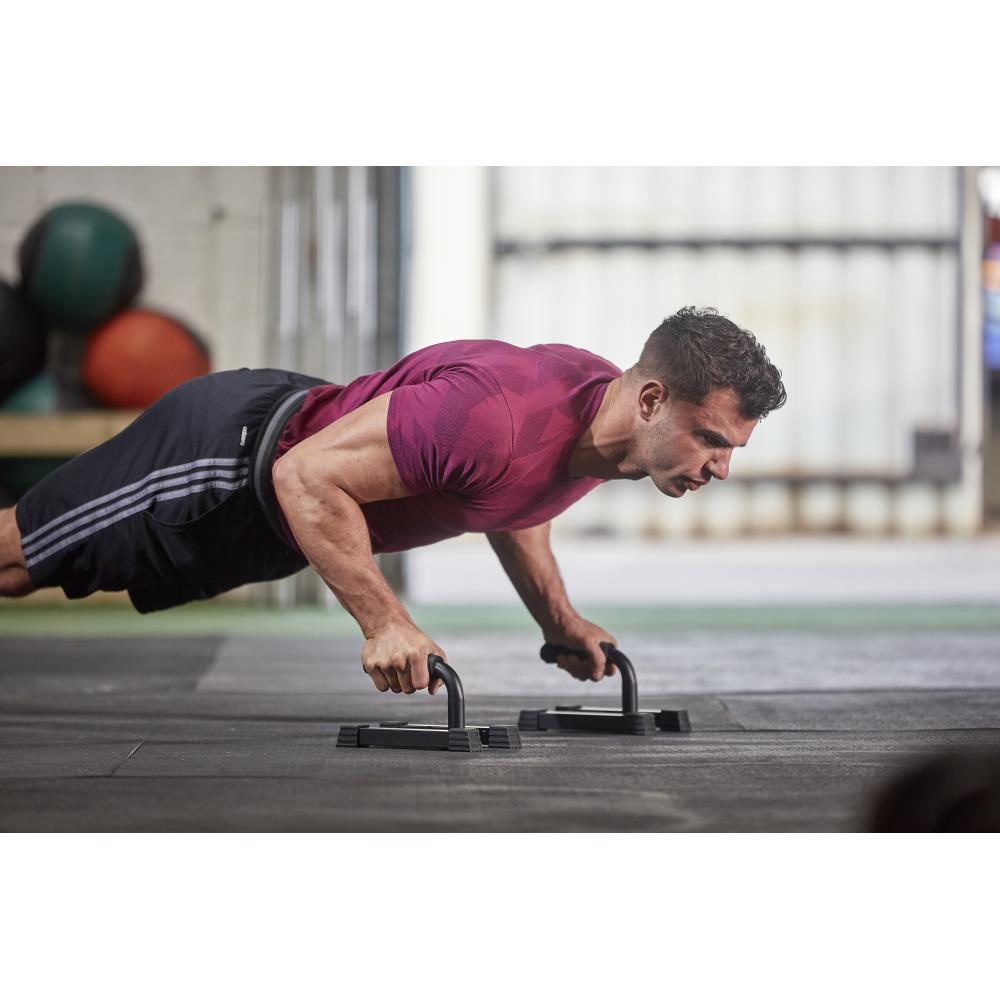 Man performing push-ups using the Adidas Premium Push Up Bars with gym equipment in the background