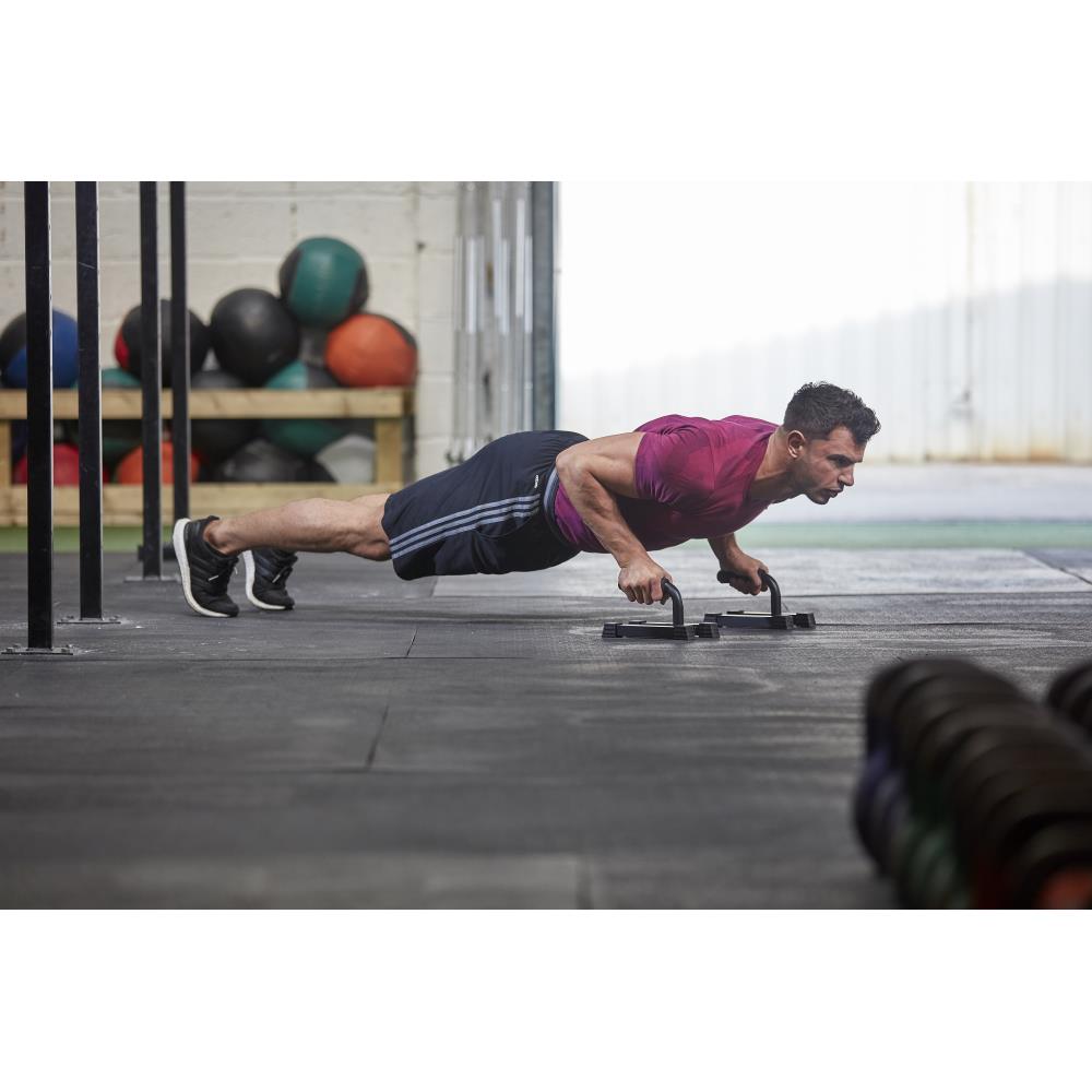 Man performing push-ups on a push-up stand in an outdoor setting with exercise balls in the background.