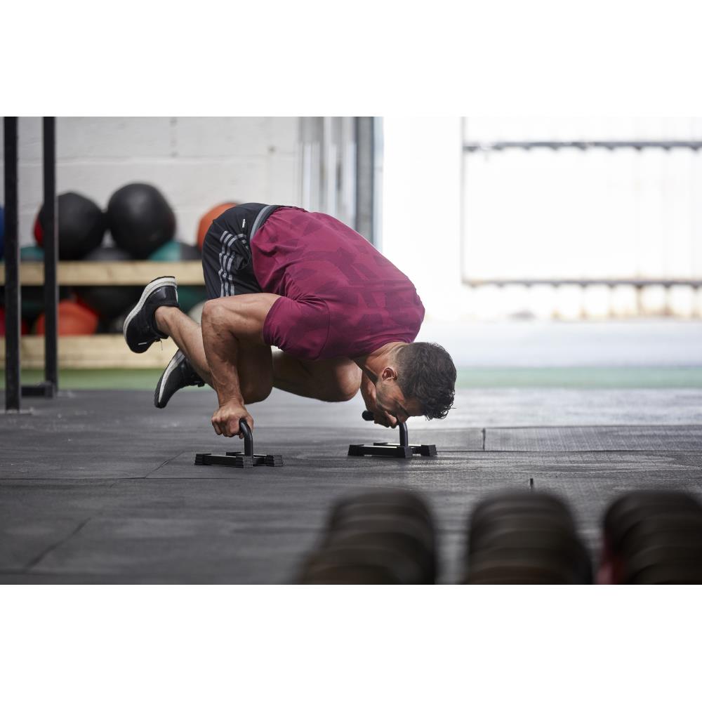 Person performing a push-up exercise with adidas push up bars on a gym floor.