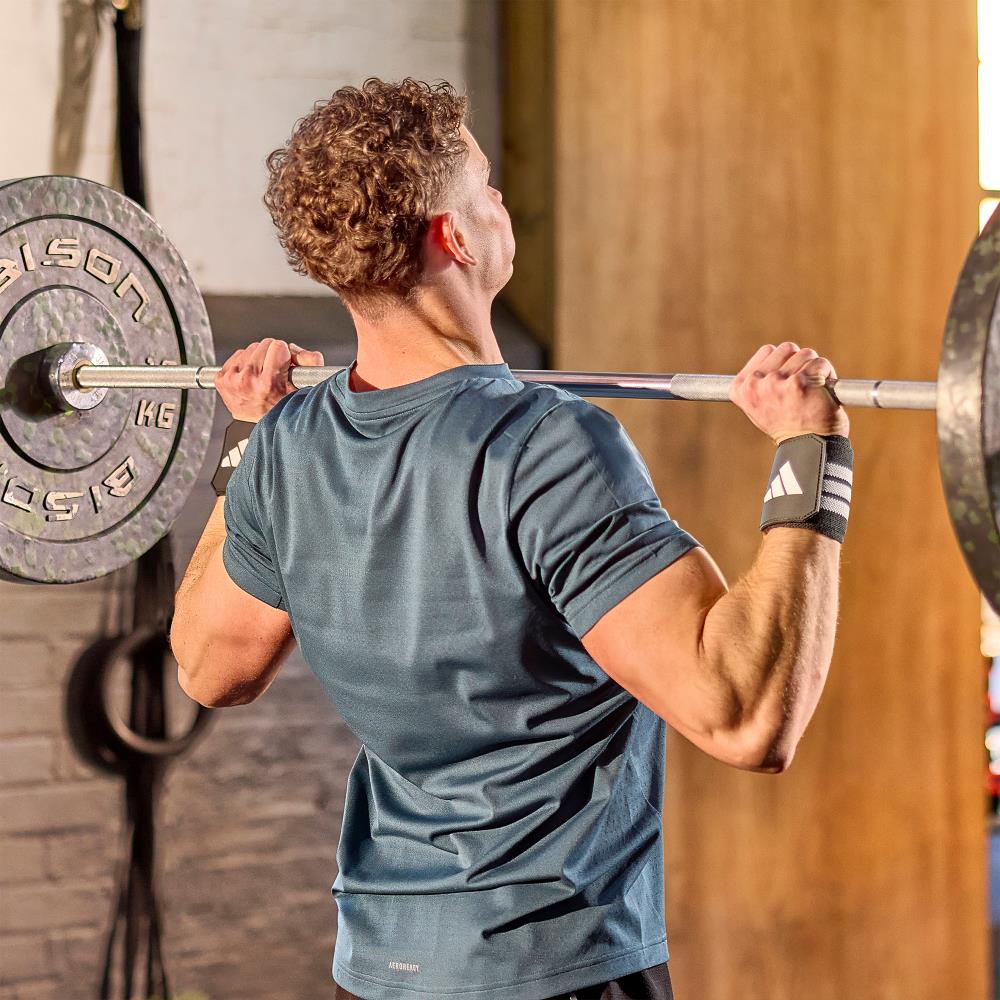 Man lifting a barbell in a gym setting wearing  adidas wrist wraps