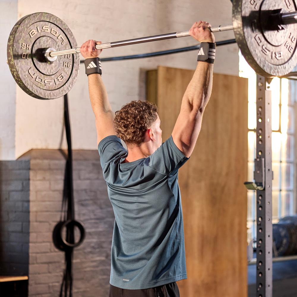 Man lifting a barbell with weights in a gym setting wearing  adidas wrist wraps