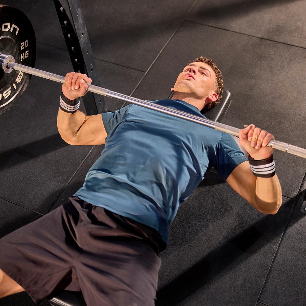 Man performing a bench press with a barbell in a gym setting wearing  adidas wrist wraps