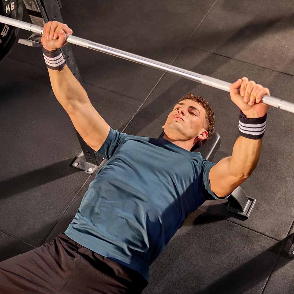 Man performing a bench press with a barbell in a gym setting wearing  adidas wrist wraps