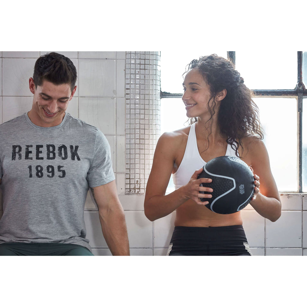 Man wearing a Reebok shirt and woman holding a medicine ball in a gym setting