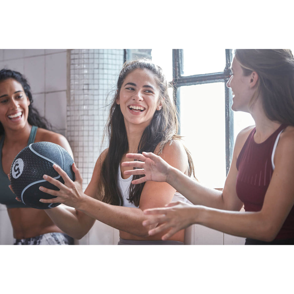 Three women in a gym setting with one holding a Reebok medicine ball.