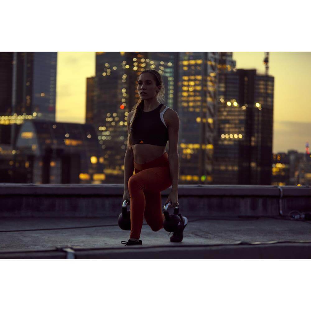 woman performing forward lunges holding two adidas 12kg kettlebells