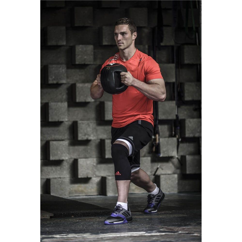 Man exercising with a slam ball whilst wearing an adidas Knee Support