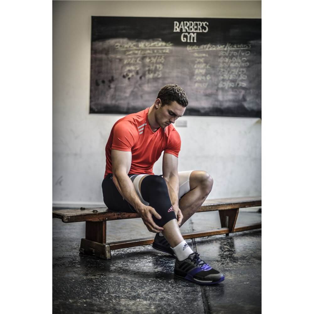 Man sitting on a gym bench adjusting his Adidas Knee Support