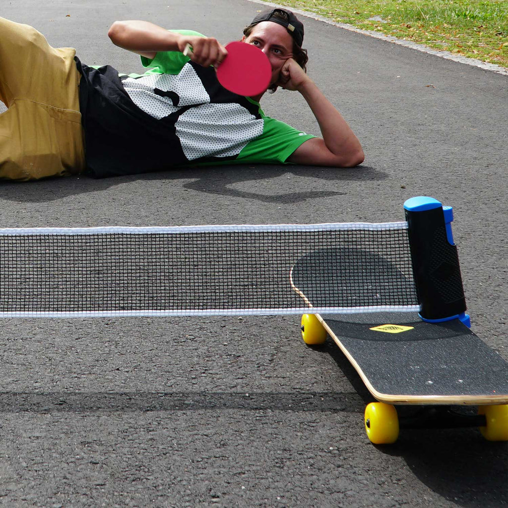 Man playing table tennis lying on the ground outside with  Donic-Schildkröt Table Tennis Net - Flexnet resting on his skateboard