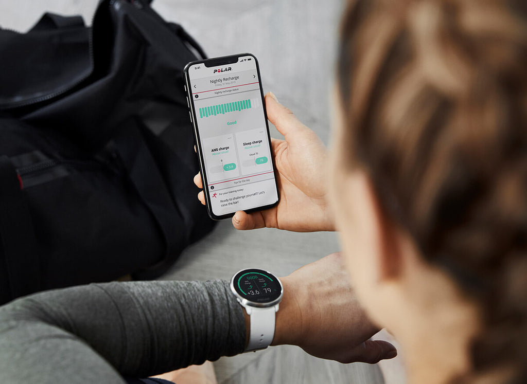 Woman wearing a white Polar Ignite Fitness Watch whilst looking at the Polar app on her phone