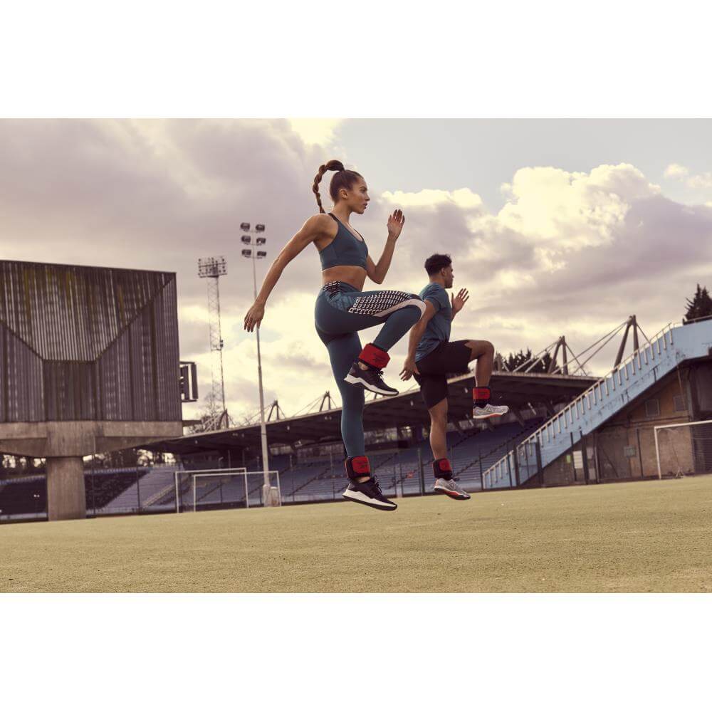 Man and woman working out on a field wearing Reebok Flexlock Ankle Weights 0.5kg