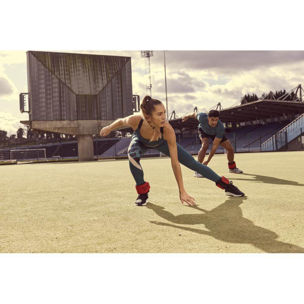 Man and woman working out on a field wearing Reebok Flexlock Ankle Weights 0.5kg