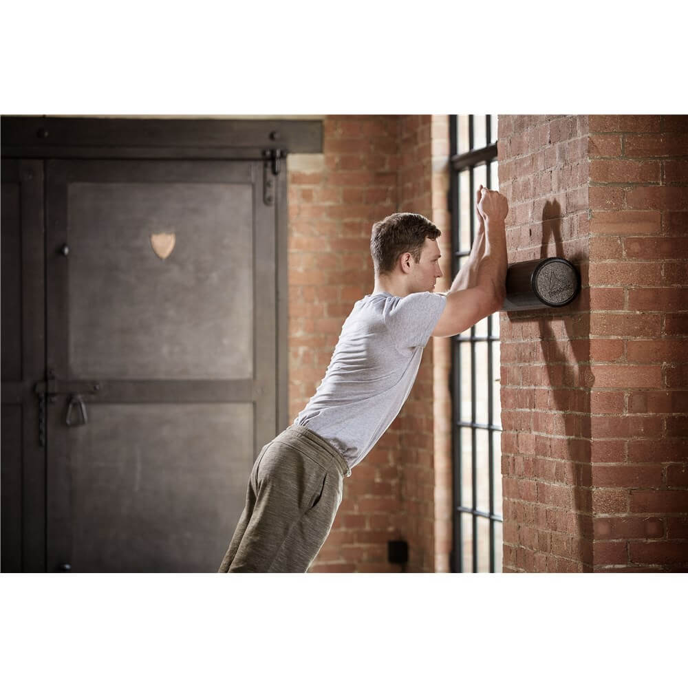 Man using Reebok Long Foam Roller against the gym wall on his arms