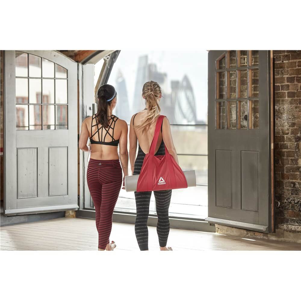 Two women at yoga class. One is holding a Reebok Mat Carry Sling with yoga mat inside it